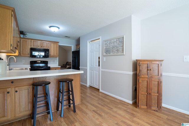 kitchen featuring a sink, light wood-style floors, black appliances, and a peninsula