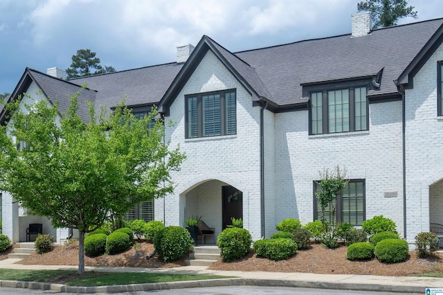 view of front of house with brick siding, a high end roof, and a chimney
