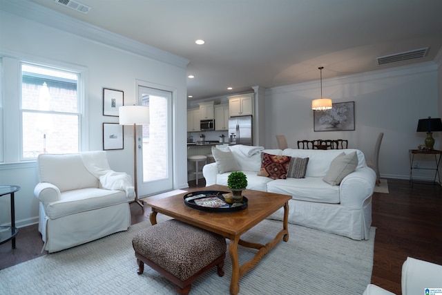 living room featuring visible vents, ornamental molding, baseboards, and wood finished floors