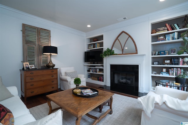 living room featuring visible vents, crown molding, wood finished floors, built in shelves, and a fireplace with flush hearth