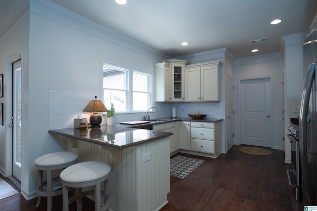 kitchen featuring a peninsula, glass insert cabinets, a sink, dark wood finished floors, and backsplash