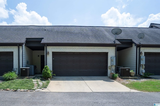multi unit property featuring brick siding, a garage, central AC unit, and concrete driveway