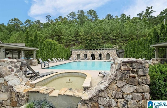 pool featuring a wooded view, a community hot tub, and a patio area