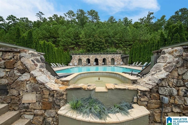community pool with a hot tub and a wooded view
