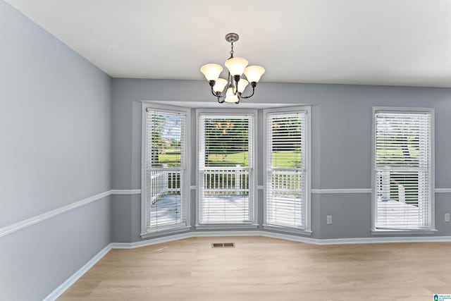 unfurnished dining area featuring an inviting chandelier, baseboards, light wood-type flooring, and visible vents