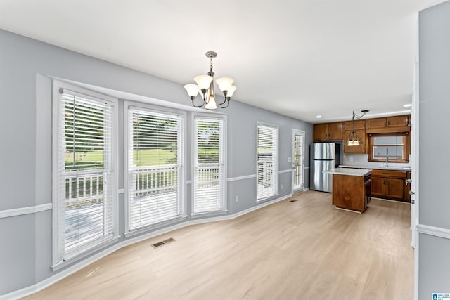 kitchen with an inviting chandelier, light wood-style flooring, freestanding refrigerator, a kitchen island, and visible vents