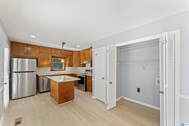 kitchen with appliances with stainless steel finishes, a sink, light wood finished floors, under cabinet range hood, and visible vents