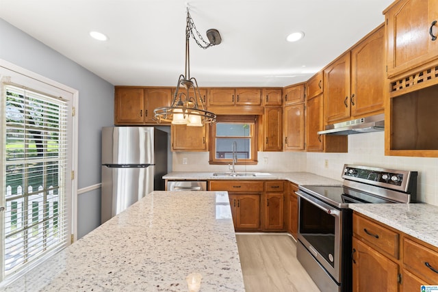 kitchen with a sink, under cabinet range hood, brown cabinets, and stainless steel appliances
