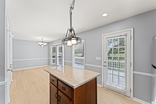 kitchen with a kitchen island, decorative light fixtures, light stone countertops, light wood-type flooring, and a chandelier