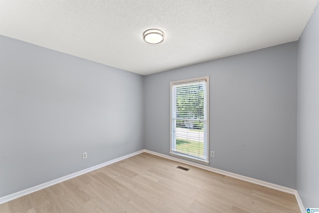 spare room with a textured ceiling, baseboards, visible vents, and light wood-type flooring