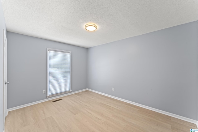 unfurnished room with light wood-type flooring, a textured ceiling, baseboards, and visible vents