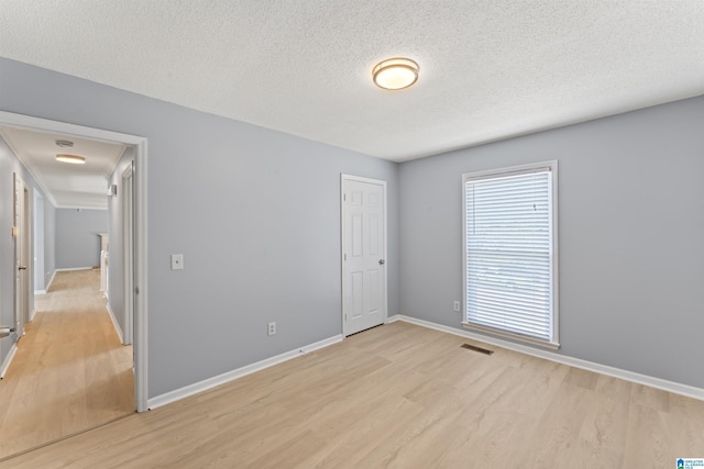 empty room featuring visible vents, a textured ceiling, light wood-style flooring, and baseboards