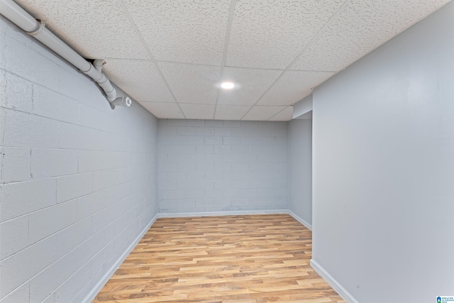 finished below grade area with concrete block wall, baseboards, a drop ceiling, and light wood-style flooring
