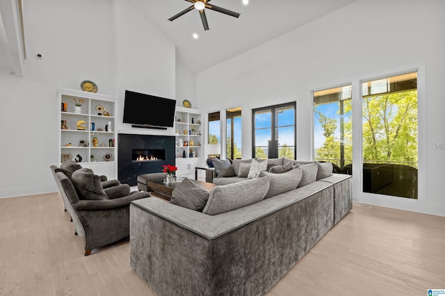 living area with high vaulted ceiling, a fireplace, light wood-style flooring, ceiling fan, and baseboards