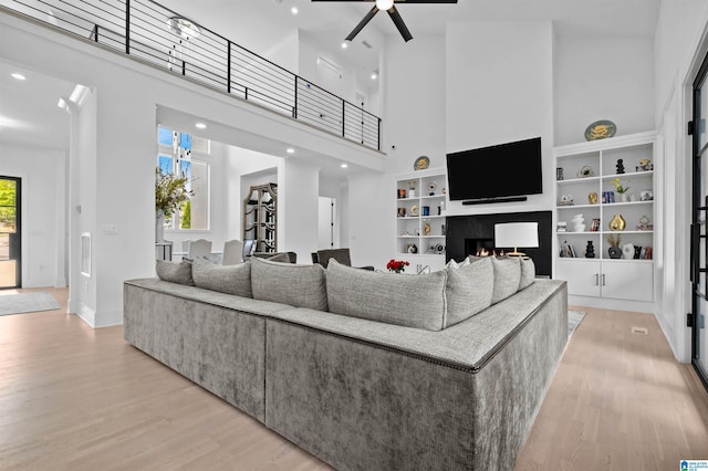 living room with a towering ceiling, light wood-style floors, ceiling fan, baseboards, and recessed lighting