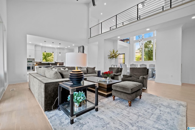living room featuring light wood-type flooring, a high ceiling, baseboards, and recessed lighting