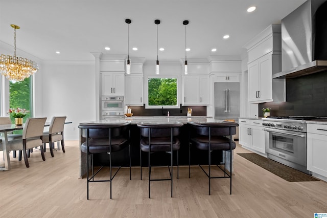 kitchen featuring premium appliances, wall chimney exhaust hood, a kitchen island, tasteful backsplash, and a chandelier
