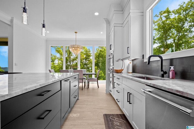 kitchen with dishwasher, a sink, a chandelier, light stone countertops, and light wood-type flooring