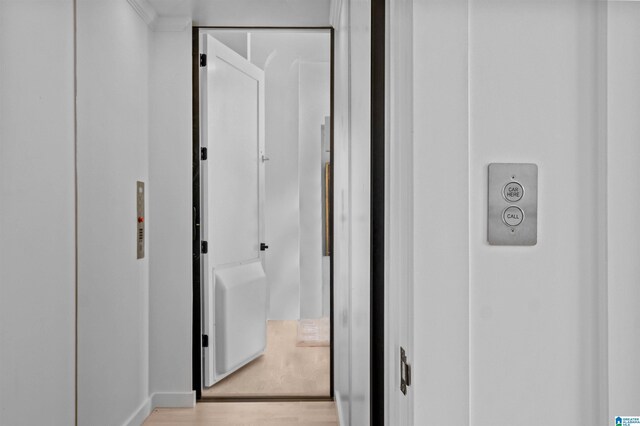 corridor with light wood-type flooring, elevator, and baseboards