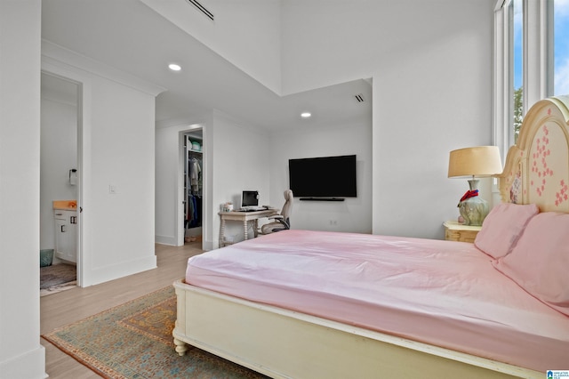 bedroom with a walk in closet, wood finished floors, recessed lighting, ensuite bathroom, and baseboards