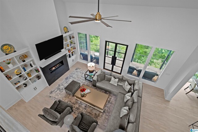 living room featuring a towering ceiling, wood finished floors, ceiling fan, and a lit fireplace