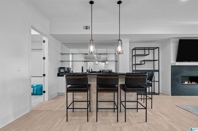 kitchen with light wood-style flooring, dark countertops, baseboards, and a glass covered fireplace