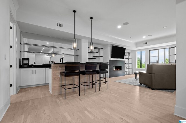 kitchen featuring light wood-style flooring, dark countertops, a breakfast bar area, white cabinets, and recessed lighting
