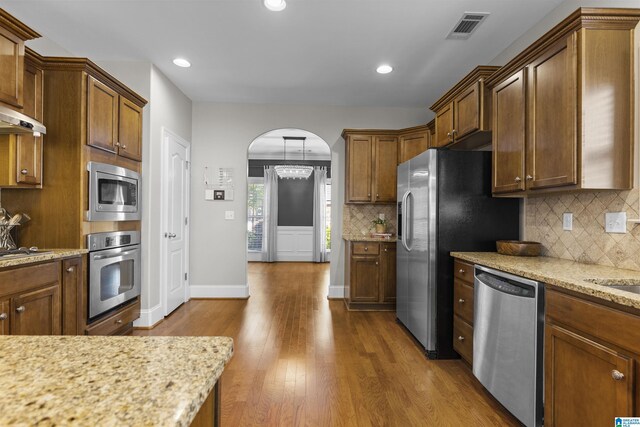 kitchen with appliances with stainless steel finishes, arched walkways, dark wood finished floors, backsplash, and visible vents