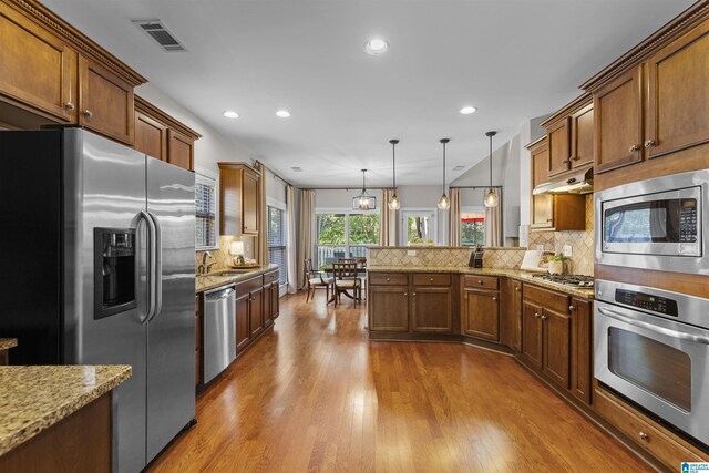 kitchen featuring appliances with stainless steel finishes, a peninsula, backsplash, visible vents, and dark wood-style floors