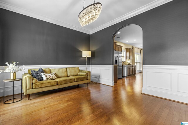 living room with an inviting chandelier, arched walkways, a wainscoted wall, wood finished floors, and ornamental molding