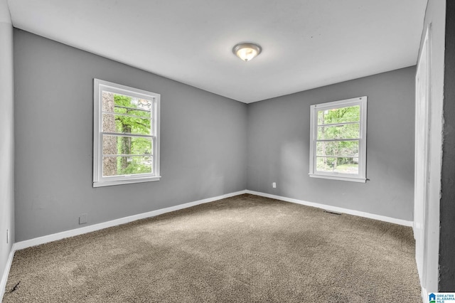 empty room featuring carpet flooring, baseboards, visible vents, and plenty of natural light