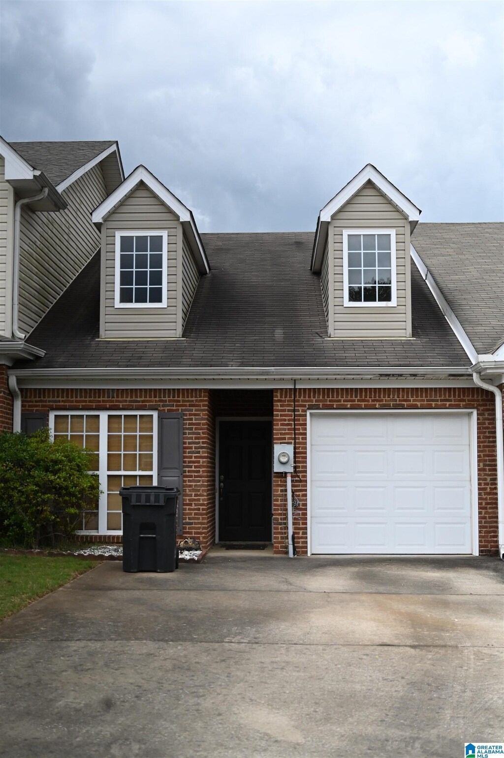 view of property with roof with shingles, an attached garage, concrete driveway, and brick siding