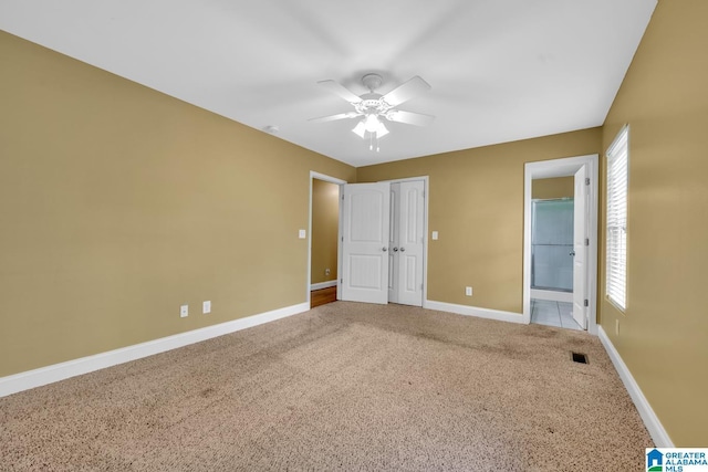 unfurnished bedroom with baseboards, carpet, ensuite bathroom, and multiple windows