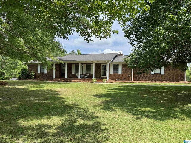 ranch-style home with covered porch, a chimney, brick siding, and a front yard