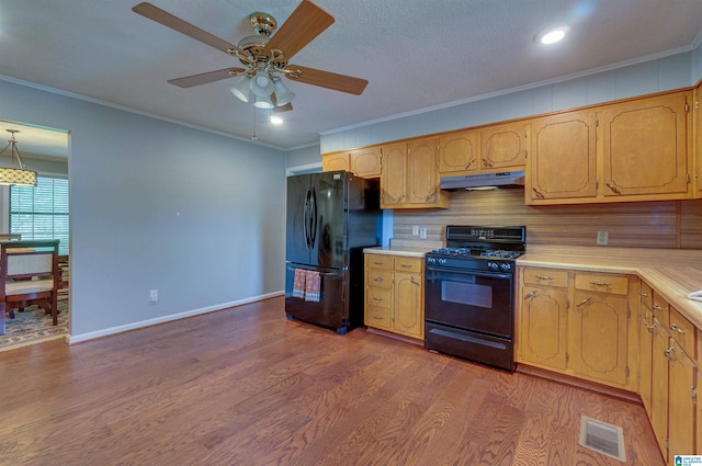 kitchen with crown molding, light countertops, under cabinet range hood, visible vents, and black appliances