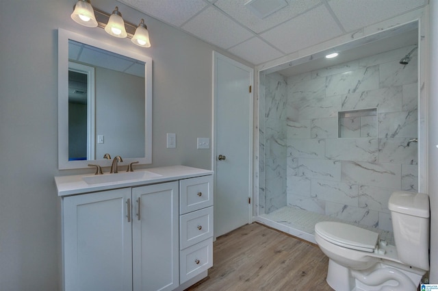 bathroom featuring vanity, wood finished floors, toilet, a drop ceiling, and tiled shower