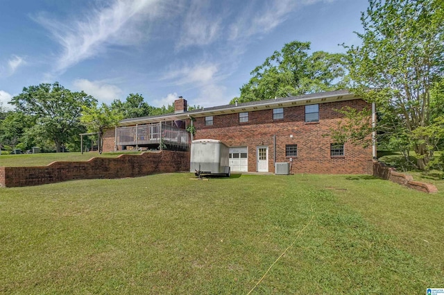 rear view of house with an attached garage, a chimney, brick siding, a lawn, and central air condition unit