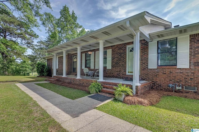 entrance to property with a porch, a yard, and brick siding