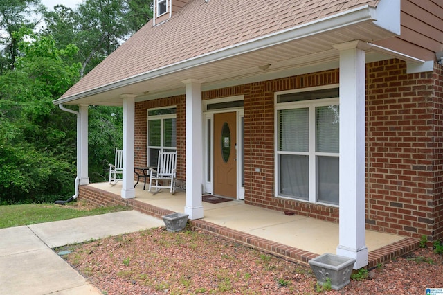 entrance to property with covered porch, a shingled roof, and brick siding