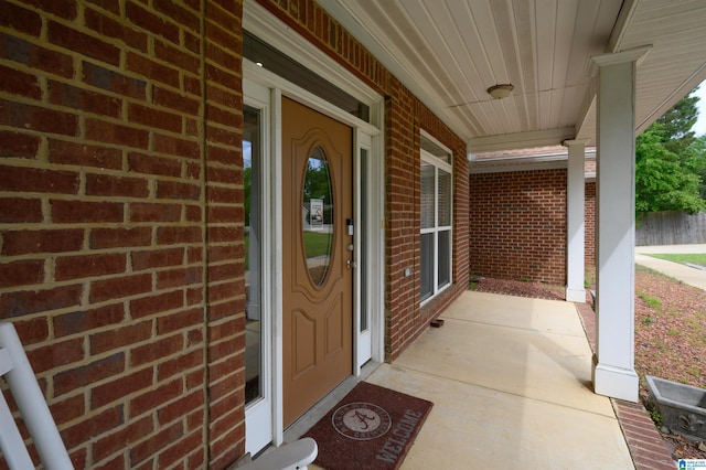 entrance to property featuring a porch and brick siding