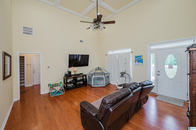 living room with ceiling fan, wood finished floors, a towering ceiling, visible vents, and coffered ceiling