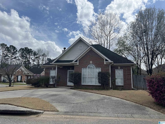 view of front facade featuring fence, a chimney, concrete driveway, and brick siding