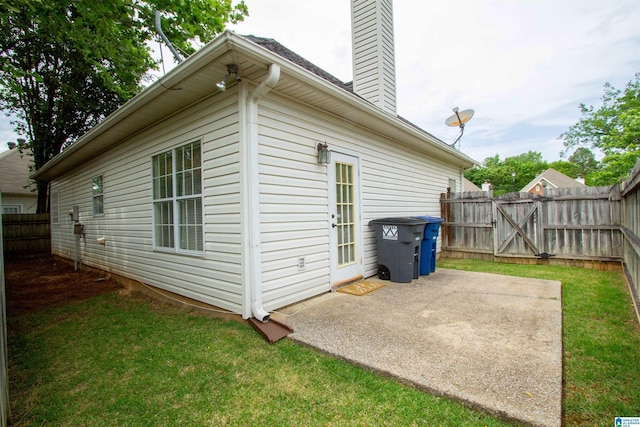 view of side of home with a yard, a patio, fence, and a chimney