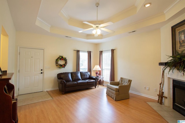 living room with crown molding, visible vents, ceiling fan, a tray ceiling, and light wood finished floors