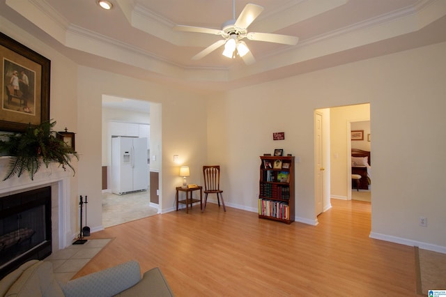 interior space featuring a ceiling fan, crown molding, a fireplace, a raised ceiling, and light wood-style flooring