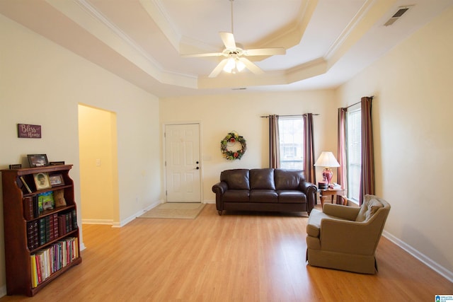 living area featuring light wood-style floors, a raised ceiling, crown molding, and a ceiling fan