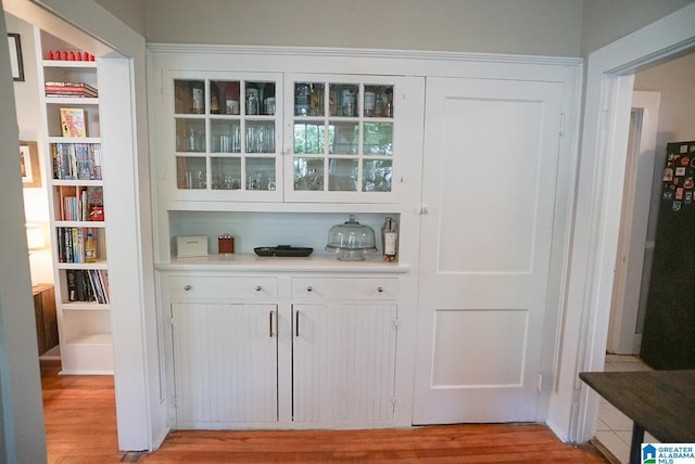 bar with freestanding refrigerator, light wood finished floors, and built in features