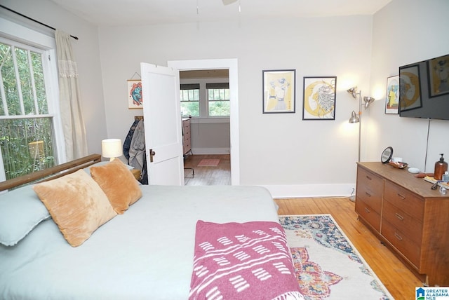 bedroom with baseboards, multiple windows, light wood-style flooring, and ensuite bath