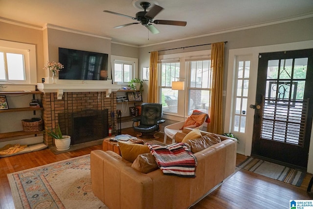 living room with crown molding, a ceiling fan, a brick fireplace, and wood finished floors