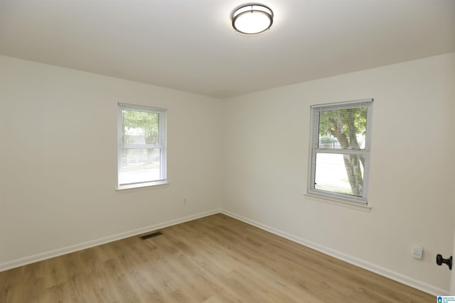 empty room featuring light wood-style floors, plenty of natural light, and visible vents